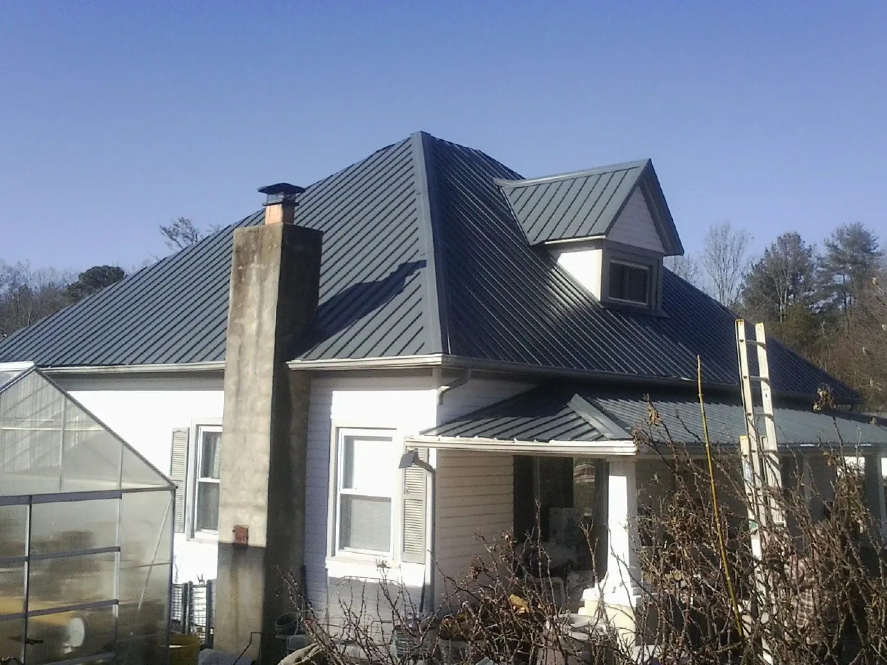 Dark blue standing seam metal roof on a white farmhouse with dormer — Slate & Tile Roof Repair by Roofing Brothers in Andrews