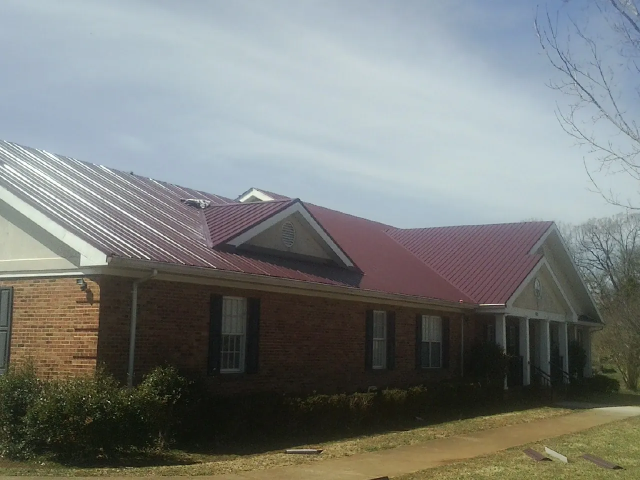 Red metal roof with gabled entries on a long brick building, from a Hail Damage Roof Repair job in Andrews