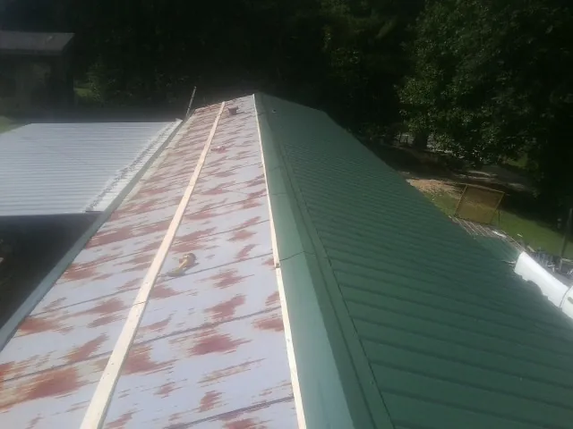 Old rusted panels beside newly installed green metal roofing — Wind Damage Roof Repair by Roofing Brothers in Andrews