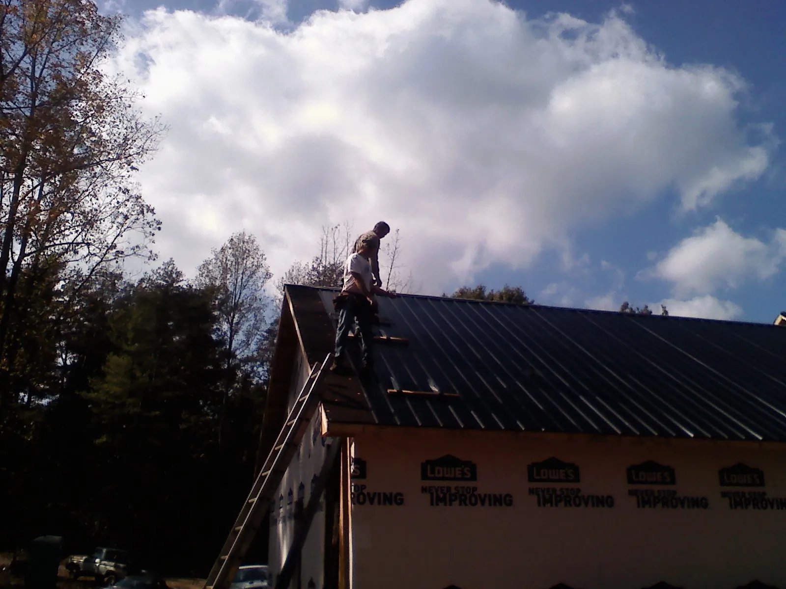 Roofer fastening dark metal panels high against a cloudy sky, from a Roof Inspection job in Andrews