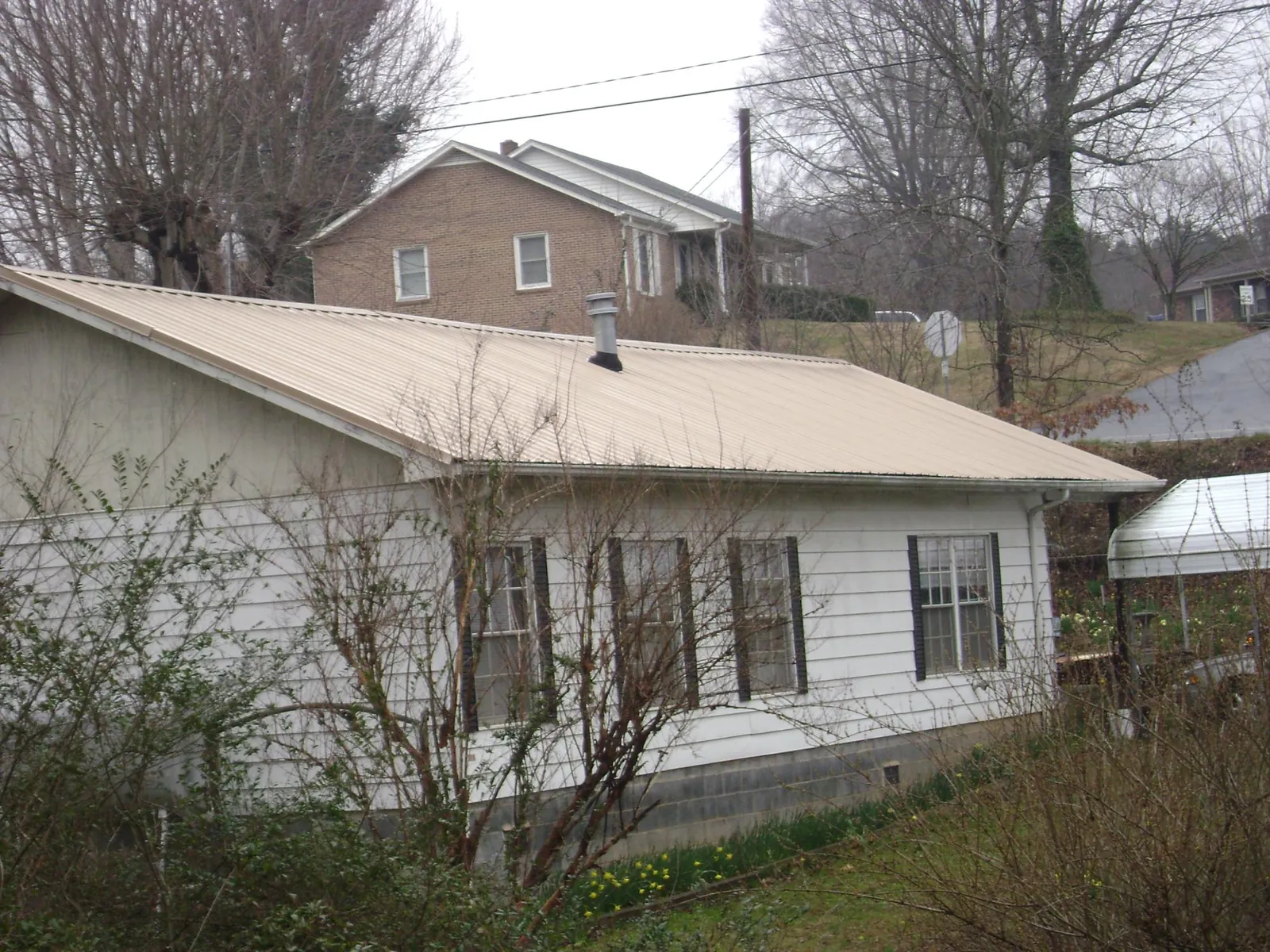 Tan metal roof on a white sided house set into a hillside — Commercial Roofing by Roofing Brothers in Andrews