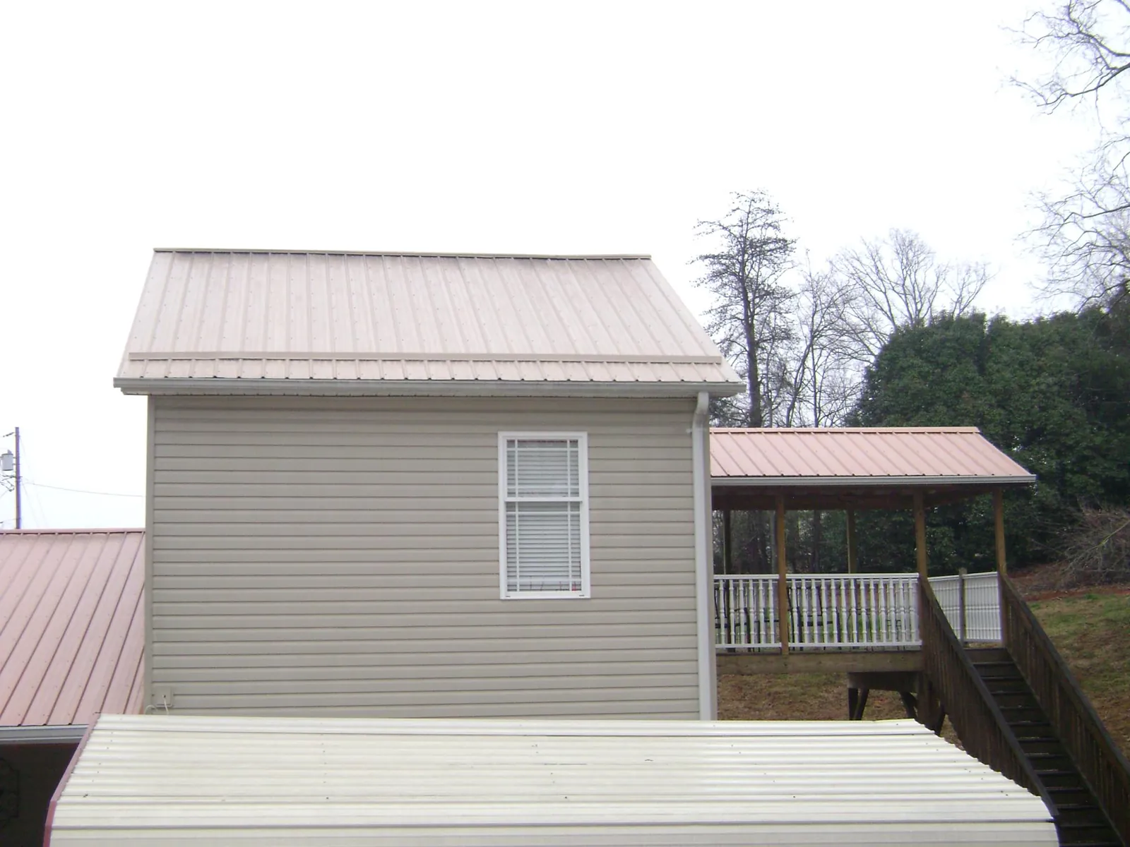 Tan metal roofs on a two story addition and attached porch, from a Roof Replacement job in Andrews